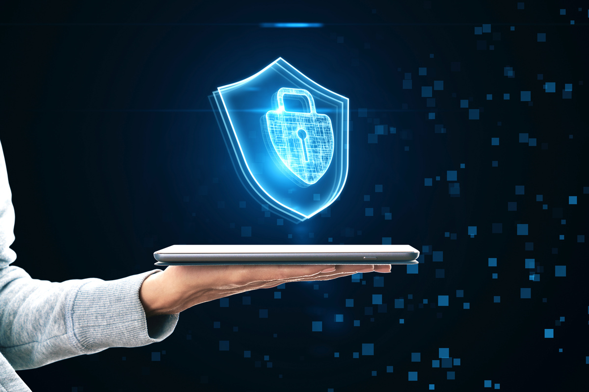 Cyber security and internet protection access concept with glowing padlock in shield symbol above human hand with digital tablet on abstract dark pixel background